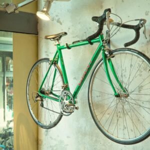 Vintage green racing bike hanging on a shop wall, showcased in an urban setting.