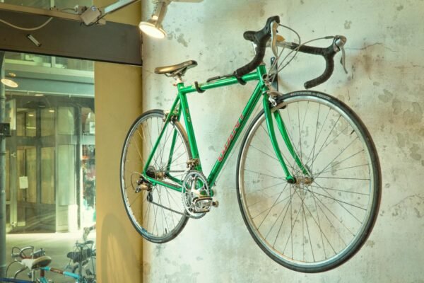 Vintage green racing bike hanging on a shop wall, showcased in an urban setting.